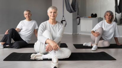 Trzy starsze osoby siedzą na macie do ćwiczeń